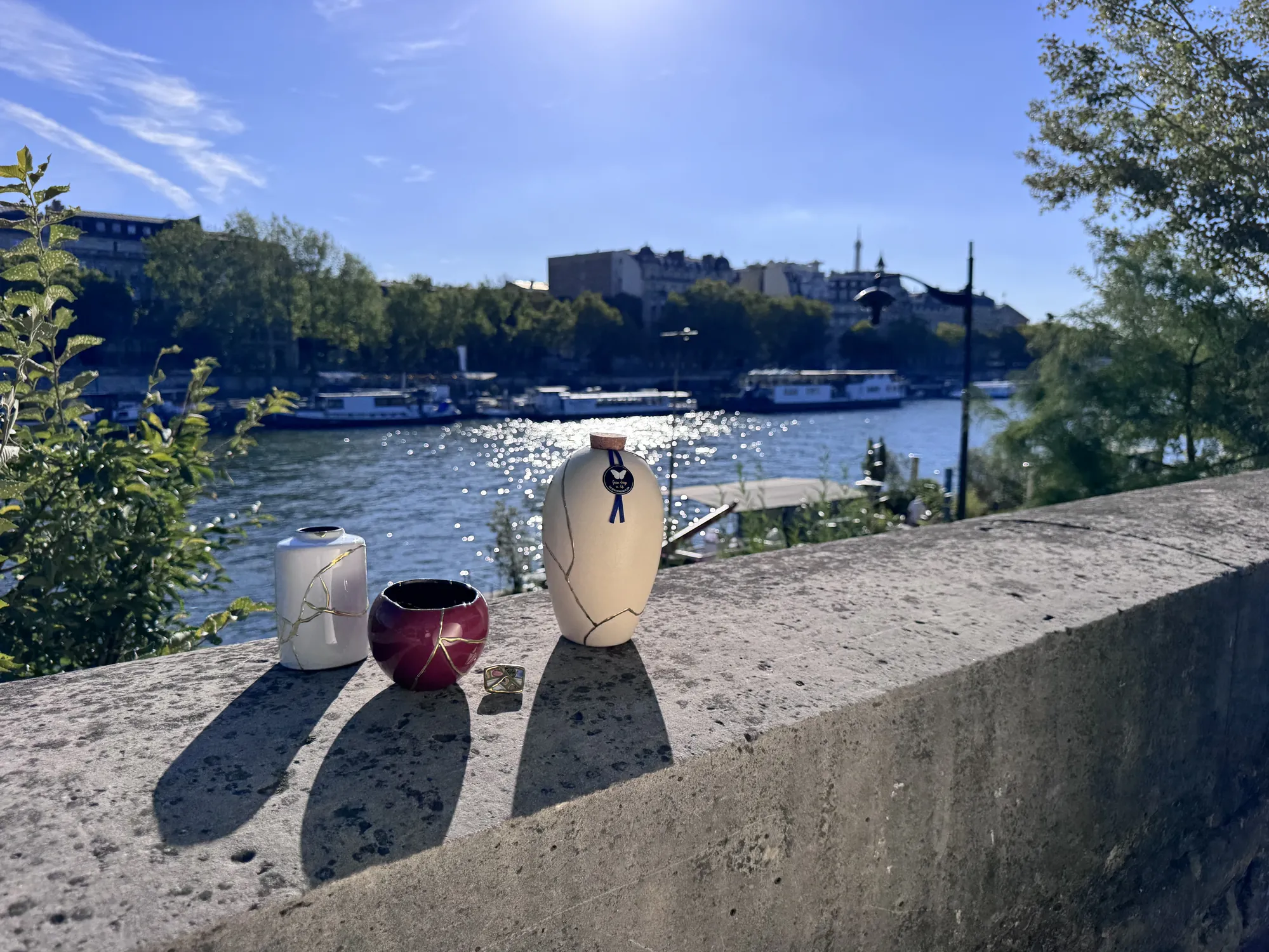 Kintsugi vaas, rode kom, broche en urn naast elkaar op een muurtje langs de Seine in Parijs Kintsugi vaas, rode kom, broche en urn naast elkaar op een muurtje langs de Seine in Parijs