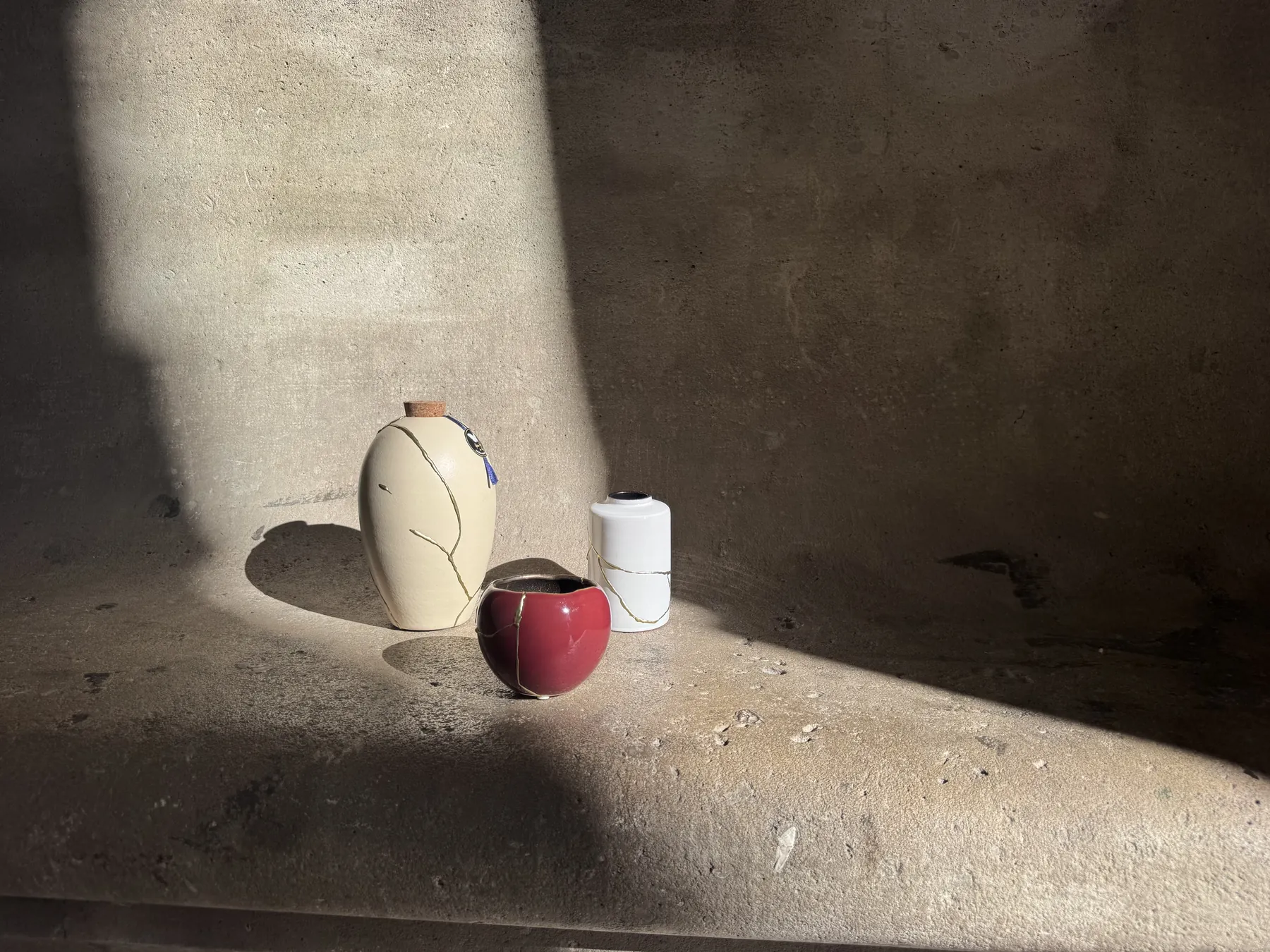 Kintsugi urn, rode kom en witte vaas in strijklicht tegen een betonnen muur in Parijs Kintsugi urn, rode kom en witte vaas in strijklicht tegen een betonnen muur in Parijs