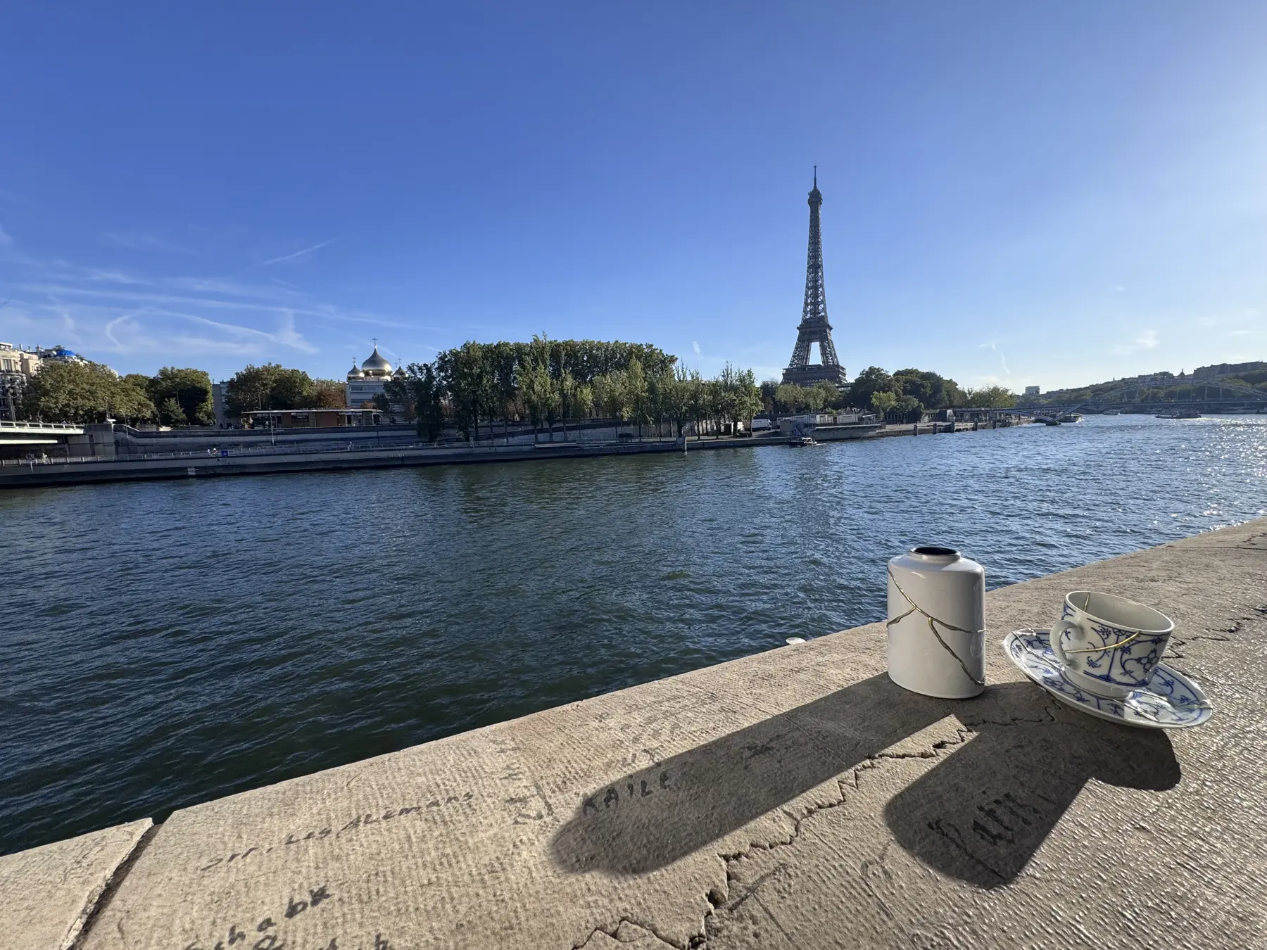 Kintsugi urn en kopje met gouden lijnen op de kade langs de Seine, met de Eiffeltoren op de achtergrond