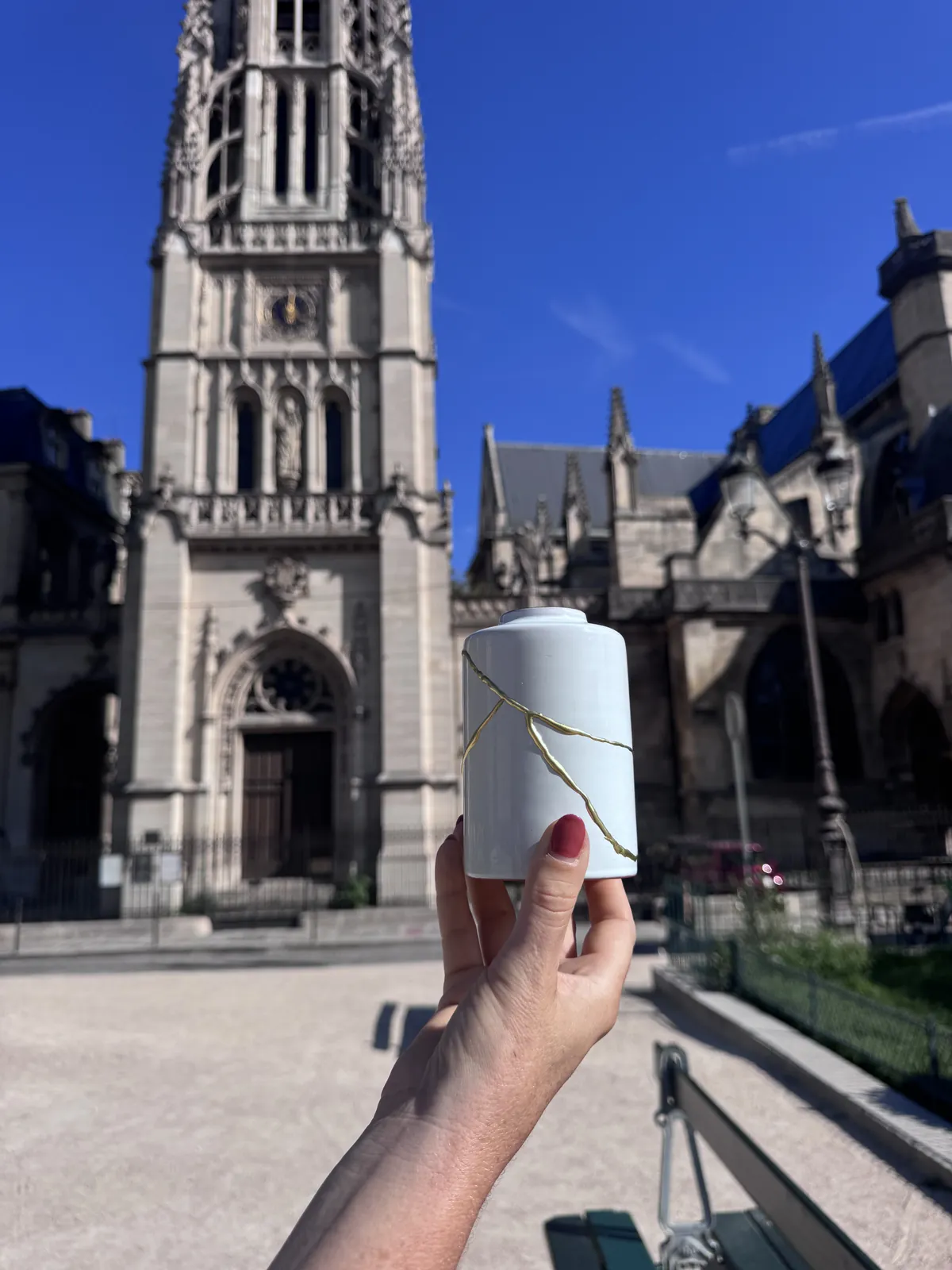 Hand met een witte Kintsugi vaas voor een kerktoren in Parijs Hand met een witte Kintsugi vaas voor een kerktoren in Parijs