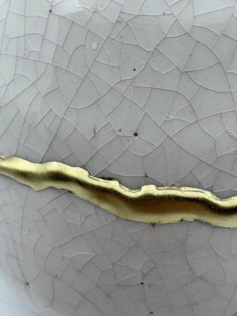 Close-up van een gouden Kintsugi-naad op wit craquelé porselein