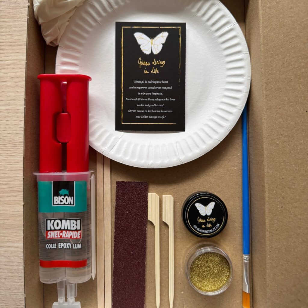 De inhoud van het Kintsugi DIY-pakket: epoxylijm, goudpigment, kwastje, schuurpapier, spatels, handschoen en een kaartje