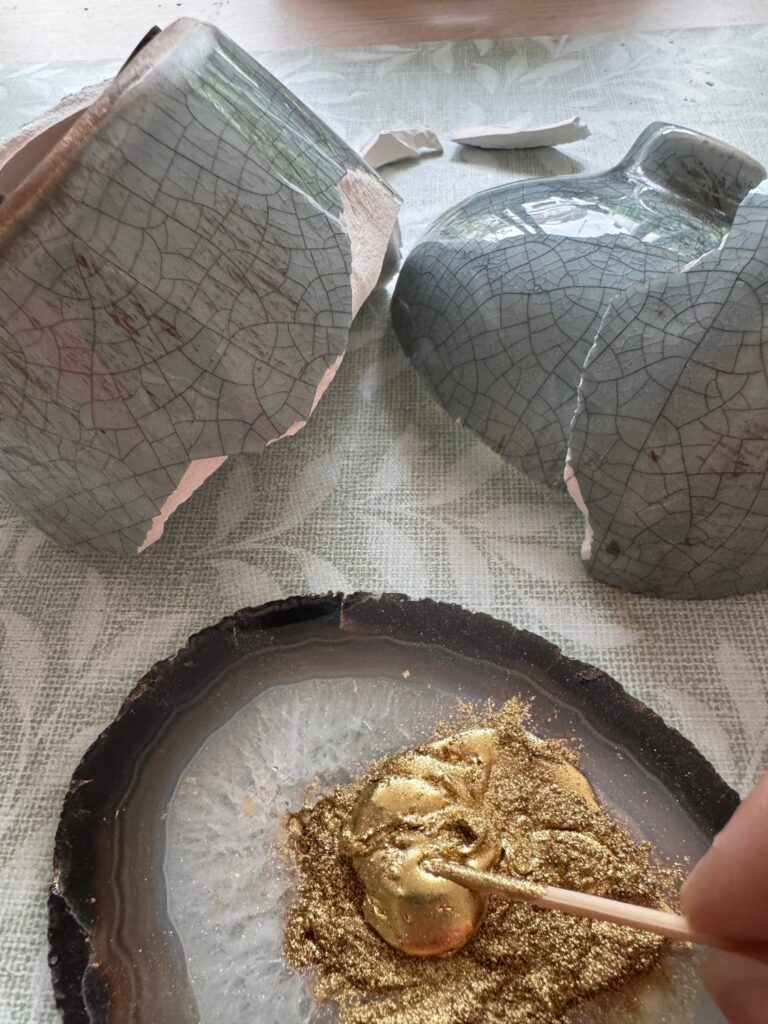 De gebroken stukken van een kom en een vaas, met op een agaatschijfje goudpigment dat wordt gemengd tot goudlijm